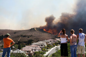 People look on as a wildfire crests a hill above a neighborhood.